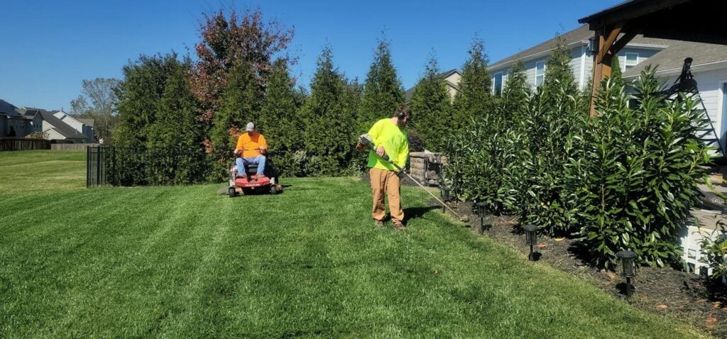 Landscaping crew mowing a lawn with a riding mower