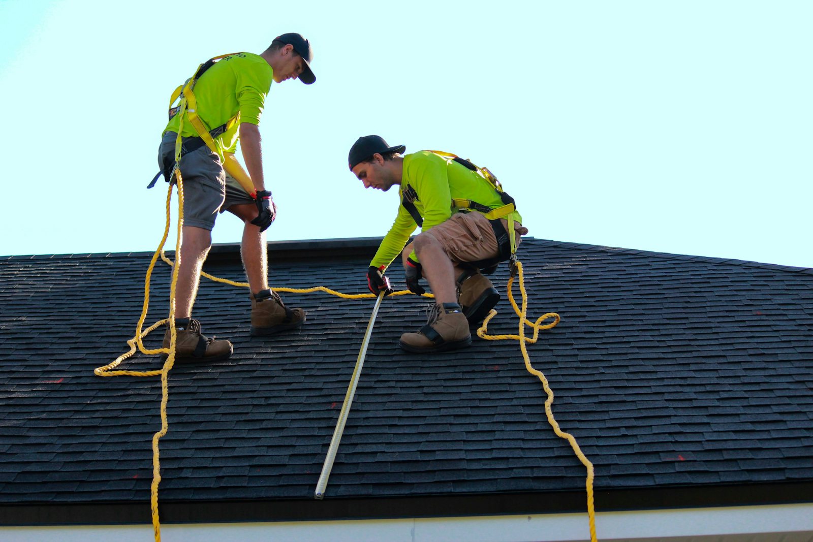 Two roofers in safety harnesses working on a shingle roof